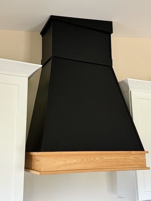 A black hood with a wooden base is hanging from the ceiling in a kitchen.