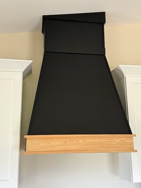 A black hood with a wooden base is hanging from the ceiling in a kitchen.