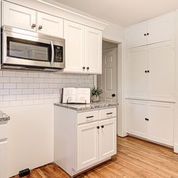 A kitchen with white cabinets , a microwave , and a refrigerator.