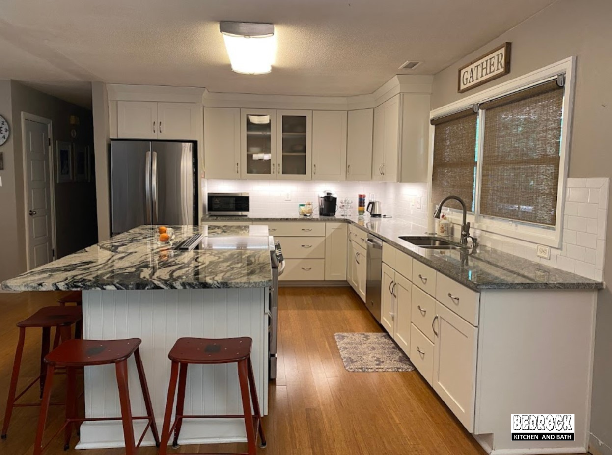 A kitchen with white cabinets , granite counter tops , stainless steel appliances and a large island.