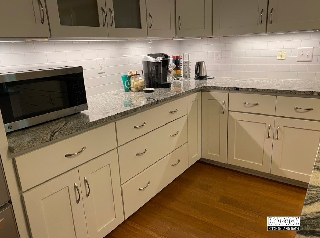 A kitchen with white cabinets , granite counter tops , and a microwave.