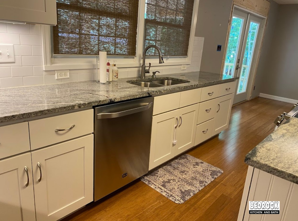 A kitchen with white cabinets , granite counter tops , a sink and a dishwasher.