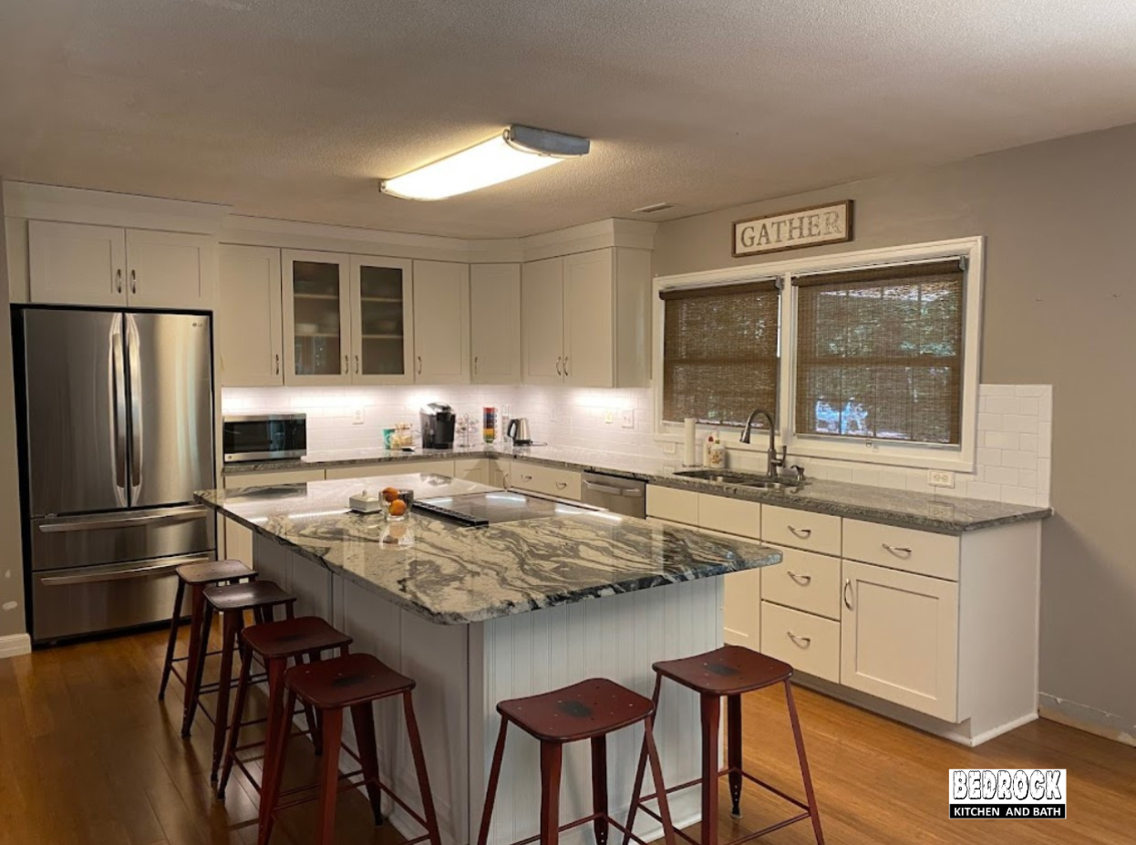 A kitchen with white cabinets , stainless steel appliances , a large island and stools.
