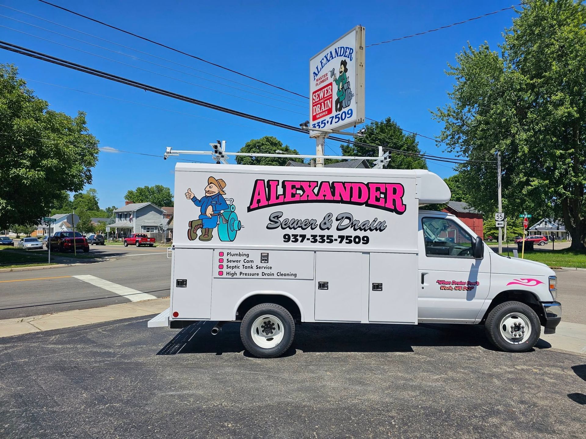 White Alexander Lawn & Dealer service truck on a street, blue sky.