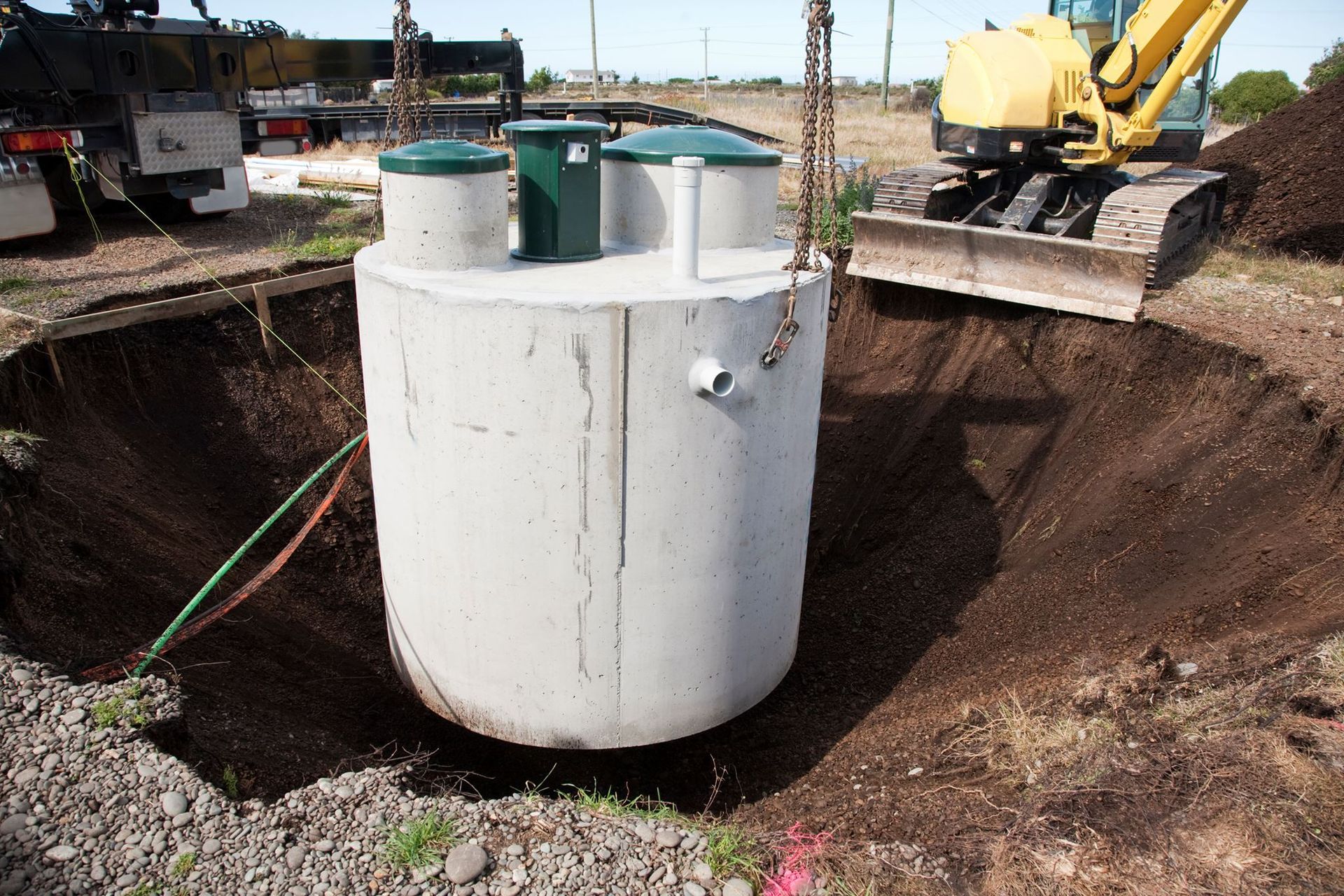 Concrete septic tank being lowered into a hole by a crane near a construction site.