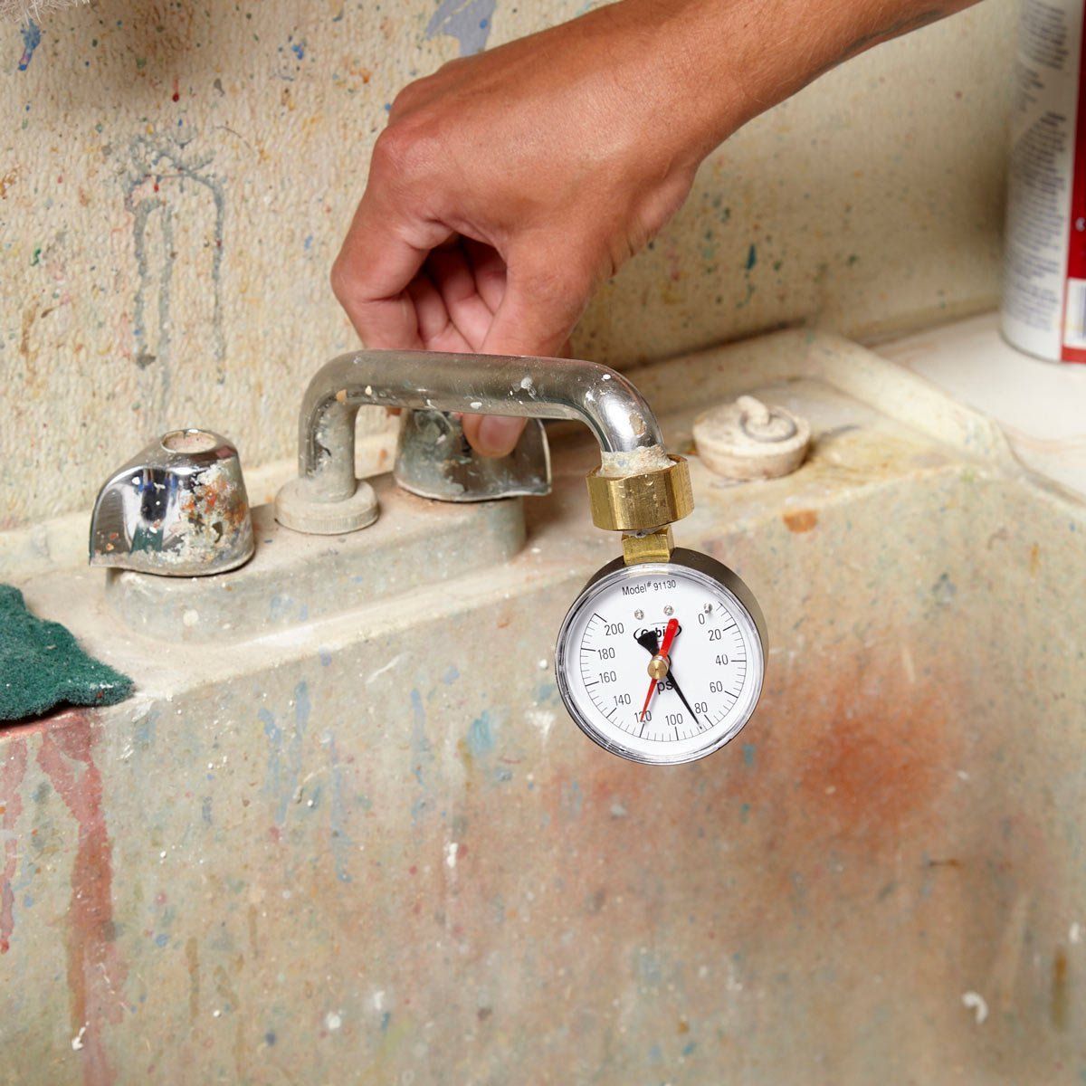 Hand turning a faucet with a pressure gauge attached in a dirty, old sink.