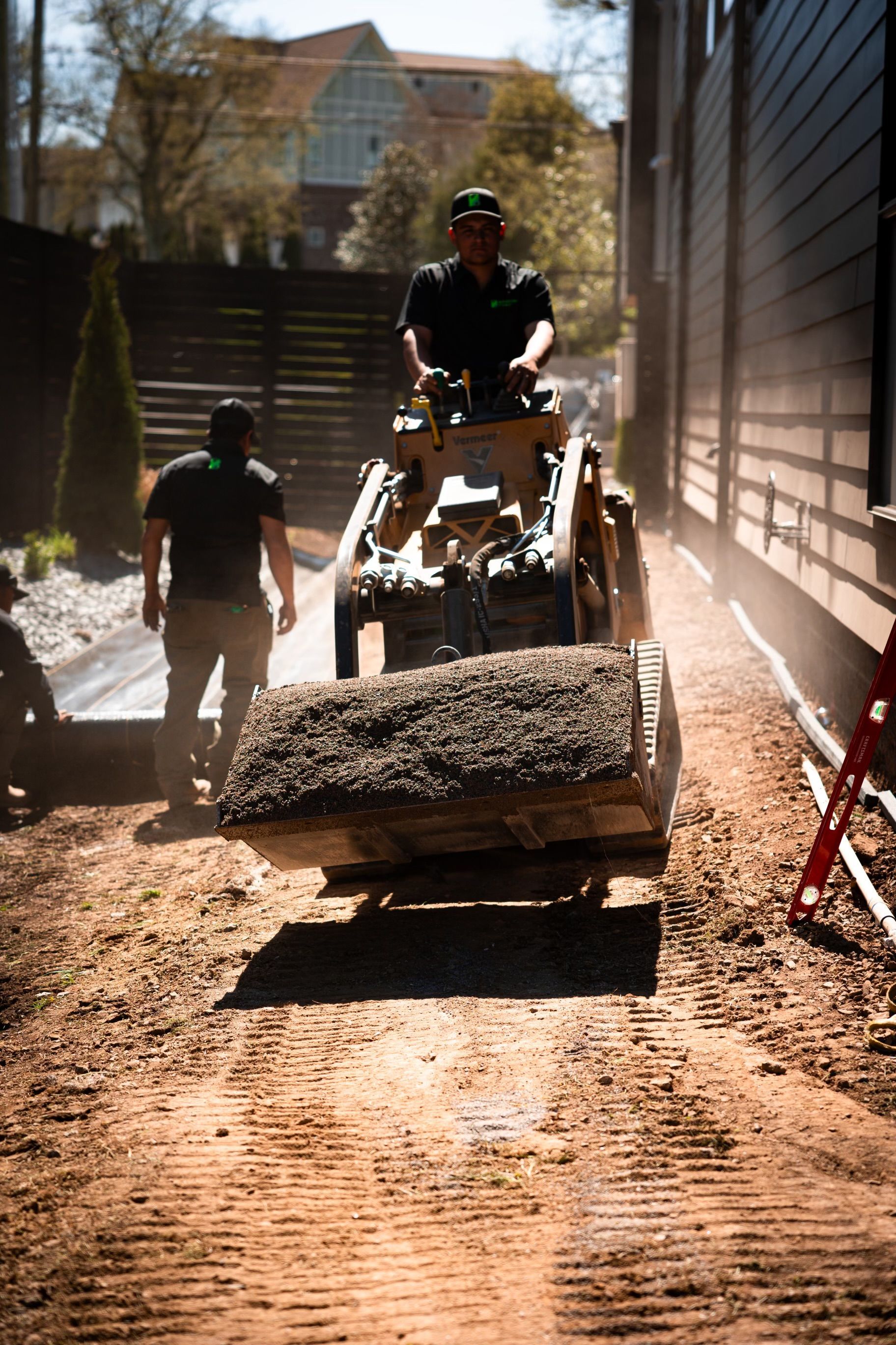 A man is driving a skid loader on a dirt road