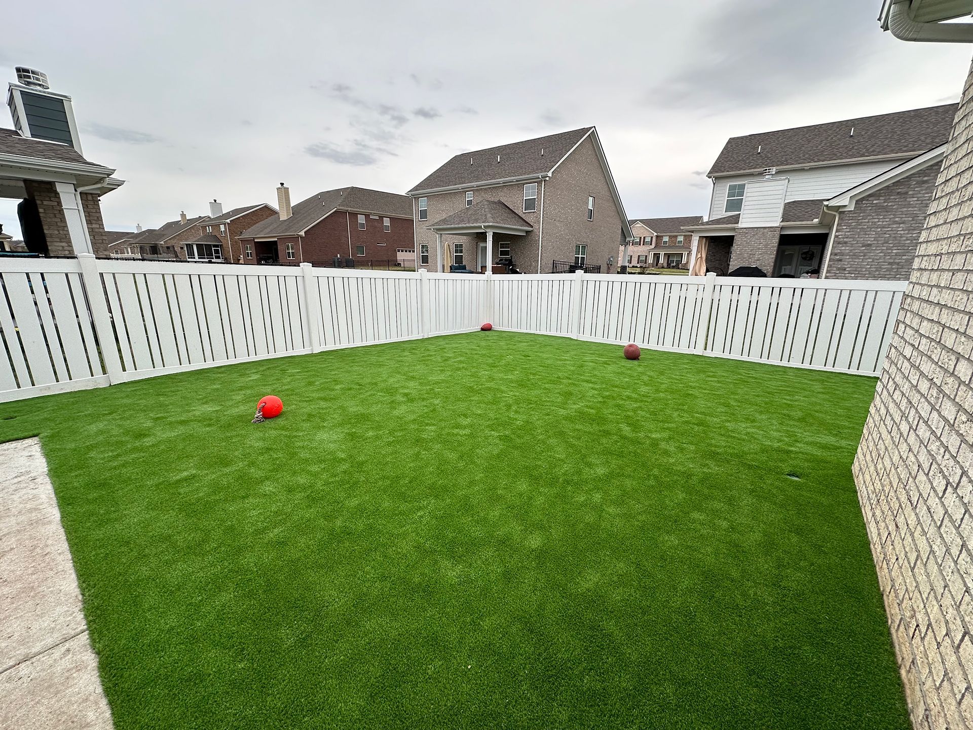 A backyard with a white fence and scattered dog toys