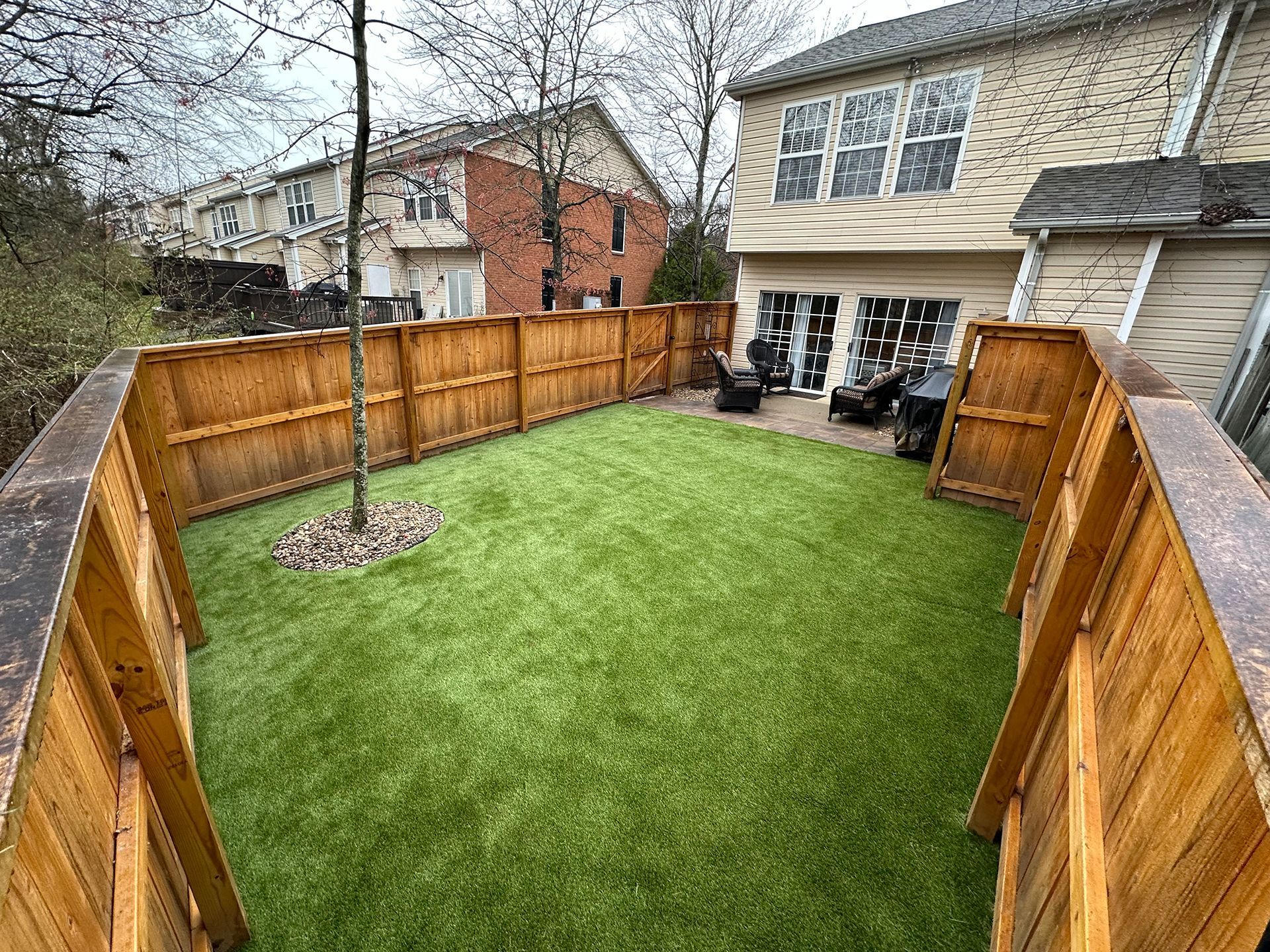 A backyard with a wooden fence and artificial grass