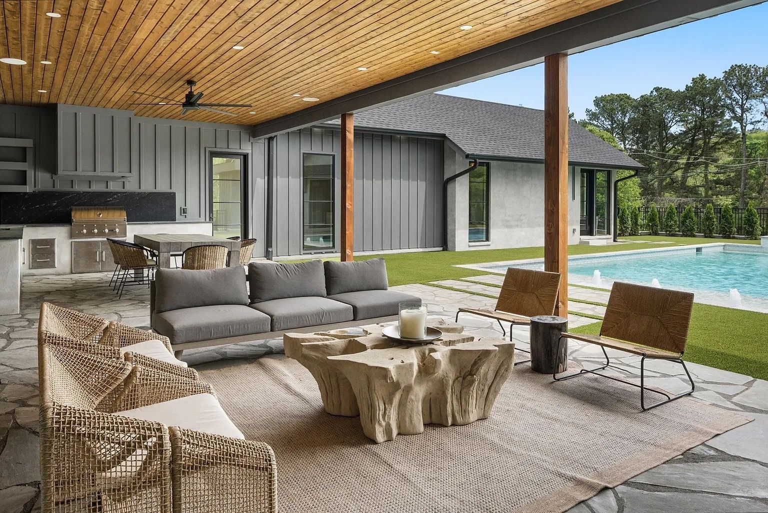 Outdoor patio with seating, kitchen, and pool, gray and wood tones.