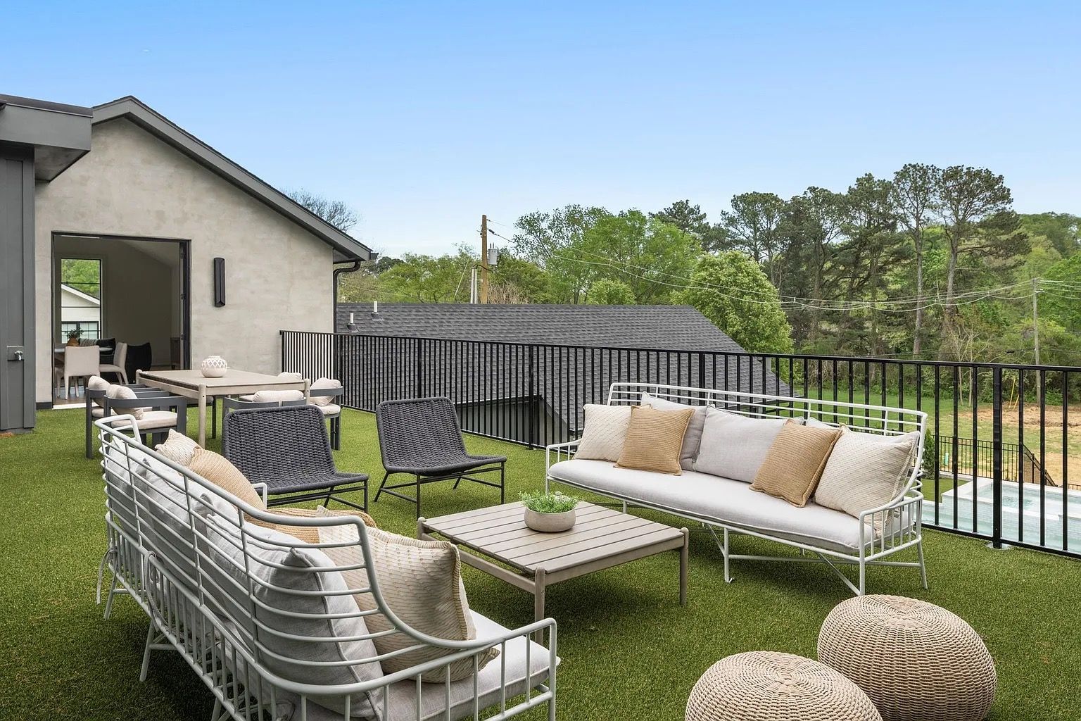Outdoor patio with white furniture, green turf, and a view of trees and a house.