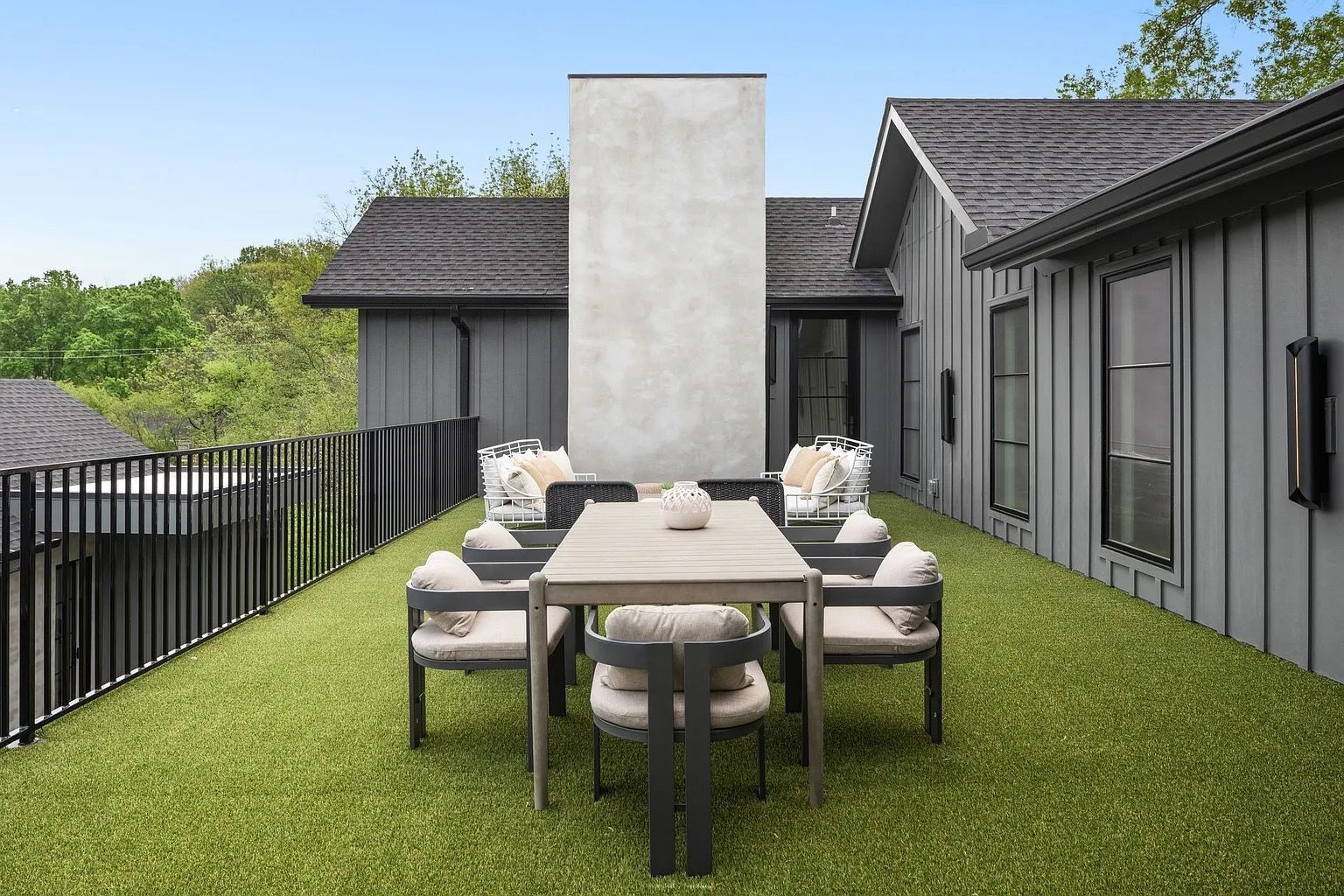 Rooftop patio with a dining table and chairs on artificial turf, next to a gray building and chimney.