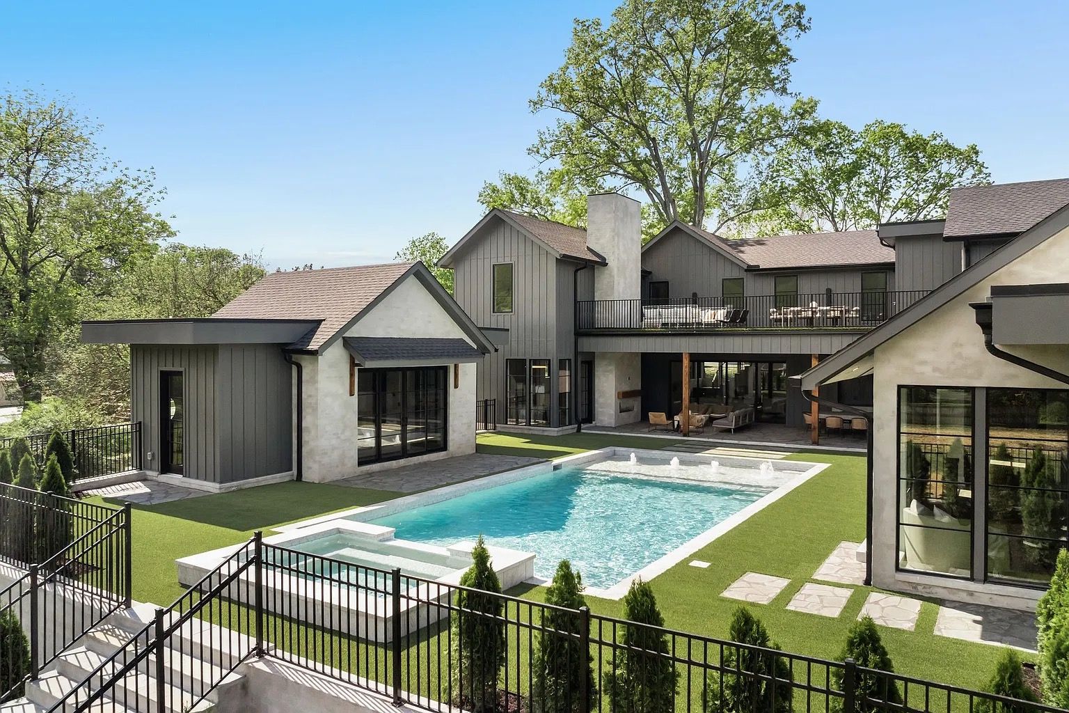 Luxurious backyard with pool and modern house. Gray and white exterior, artificial grass, sunny day.