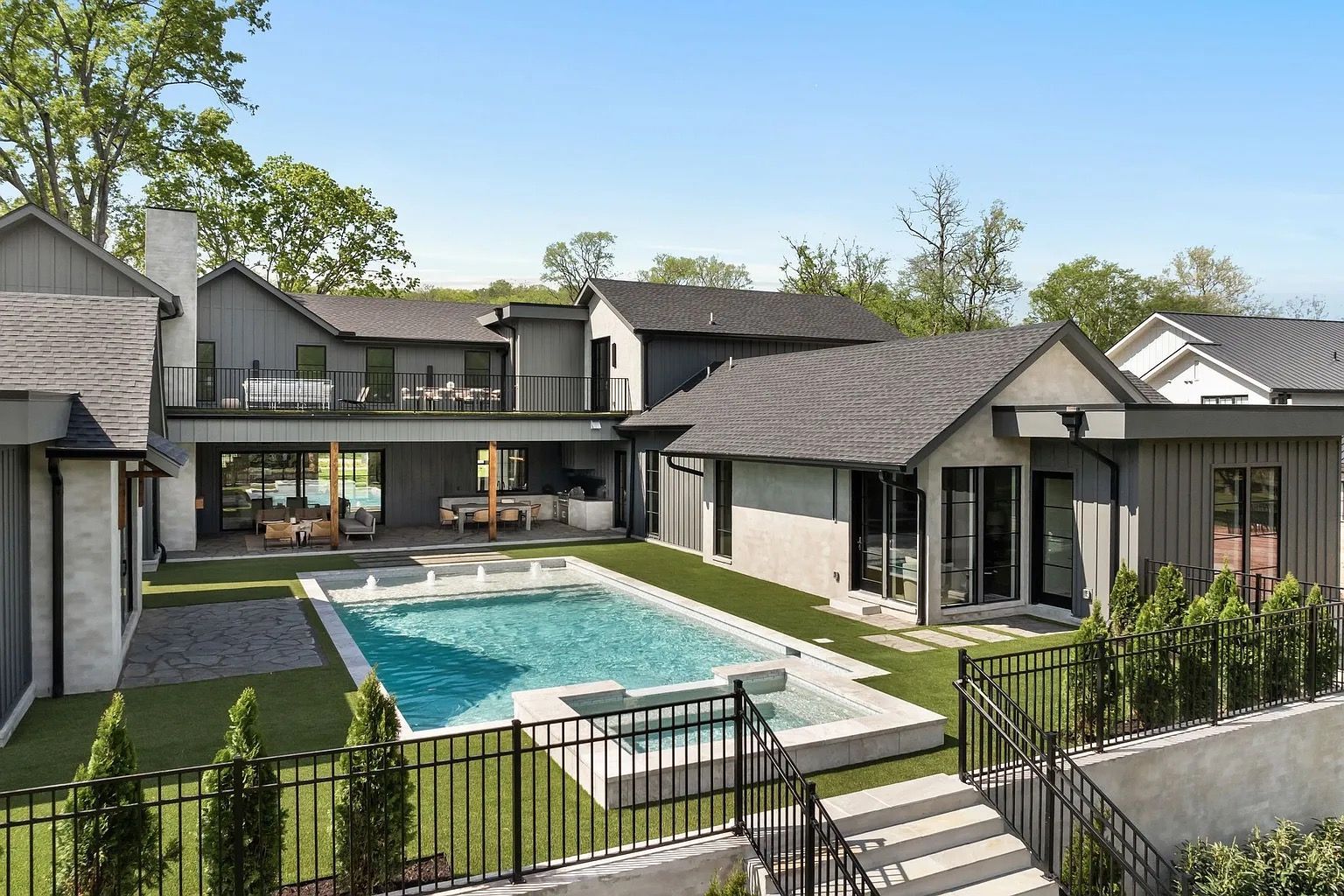 Modern gray house with pool, spa, and landscaped yard on a sunny day.