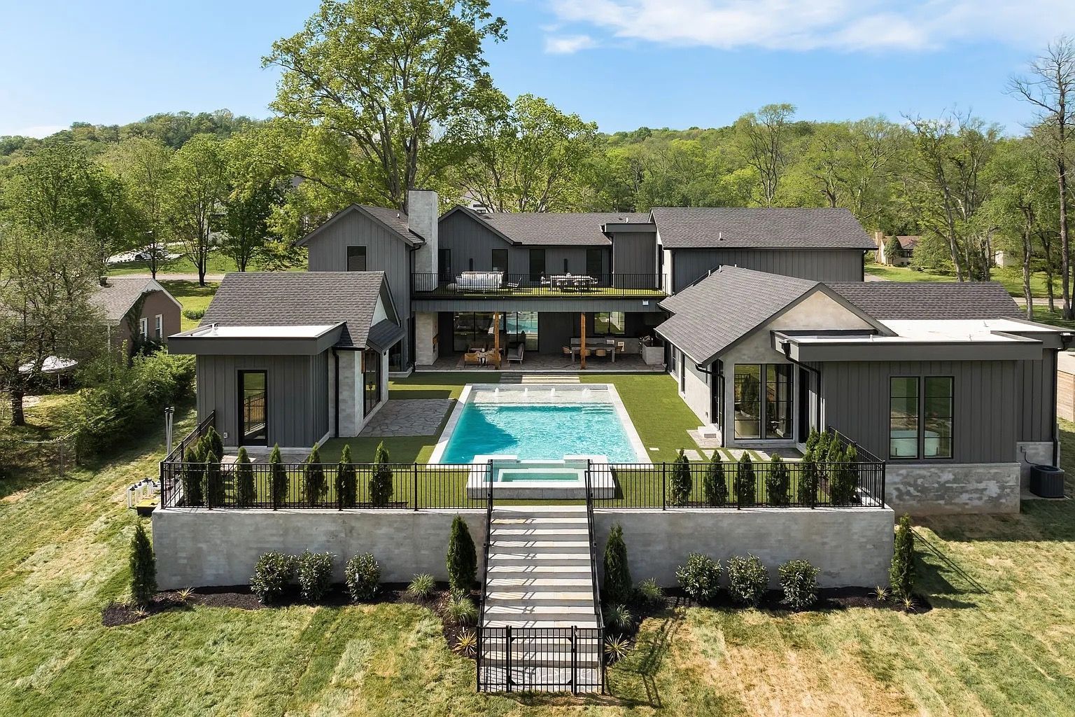 Modern house with a pool and outdoor seating area. Grey exterior, blue pool, green grass.