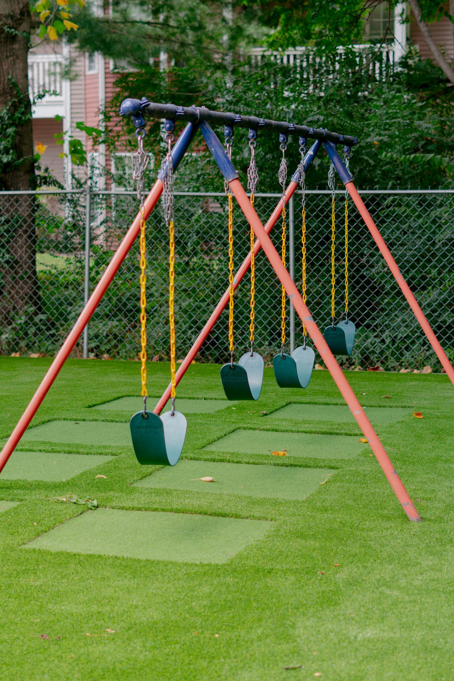 A swing set with four green swings on a green, artificial turf playground.