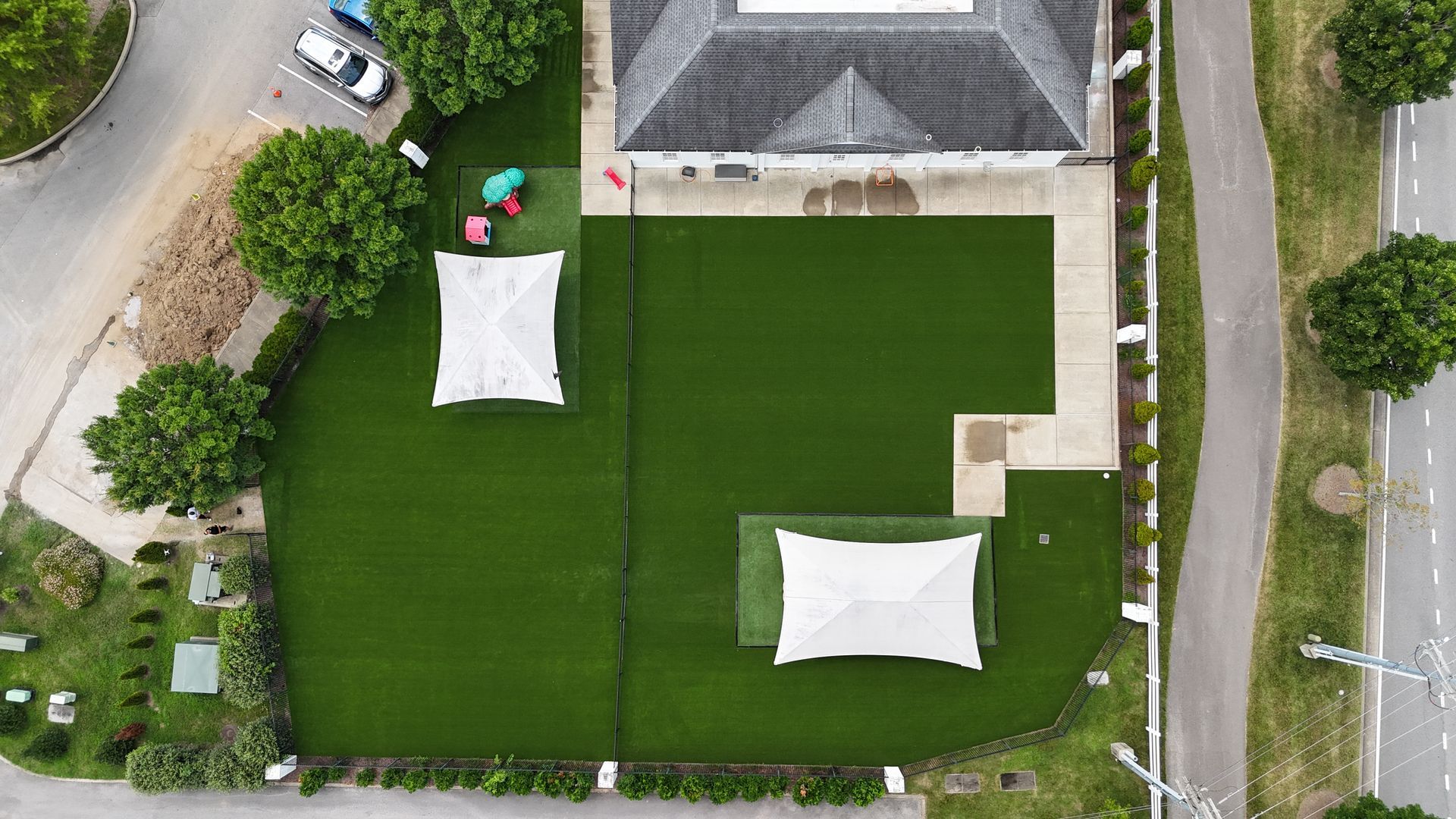Aerial view of a building with a green lawn, two white tents, and a nearby road.