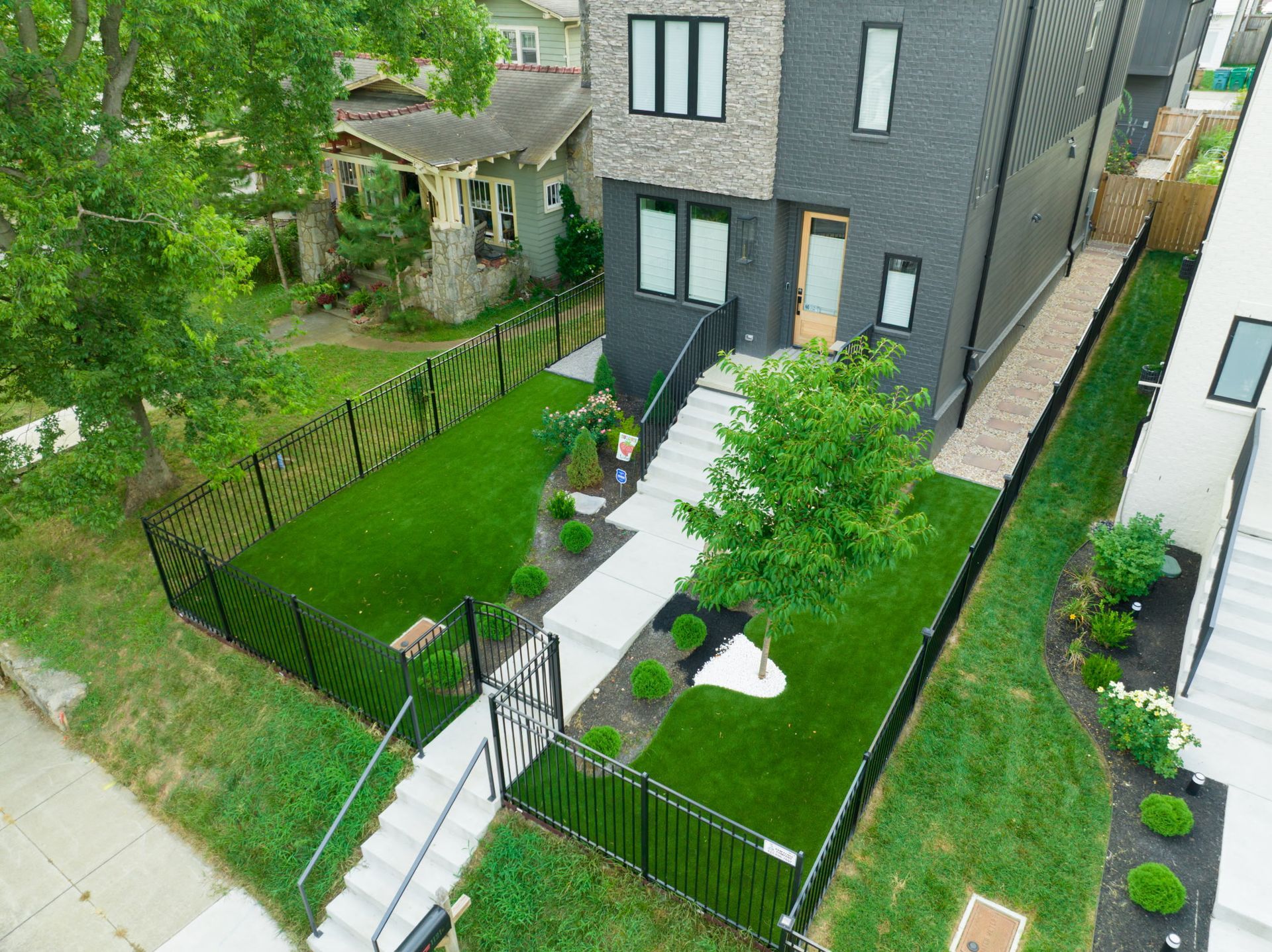 Modern home with black fence, steps to the front door, and a small green lawn.
