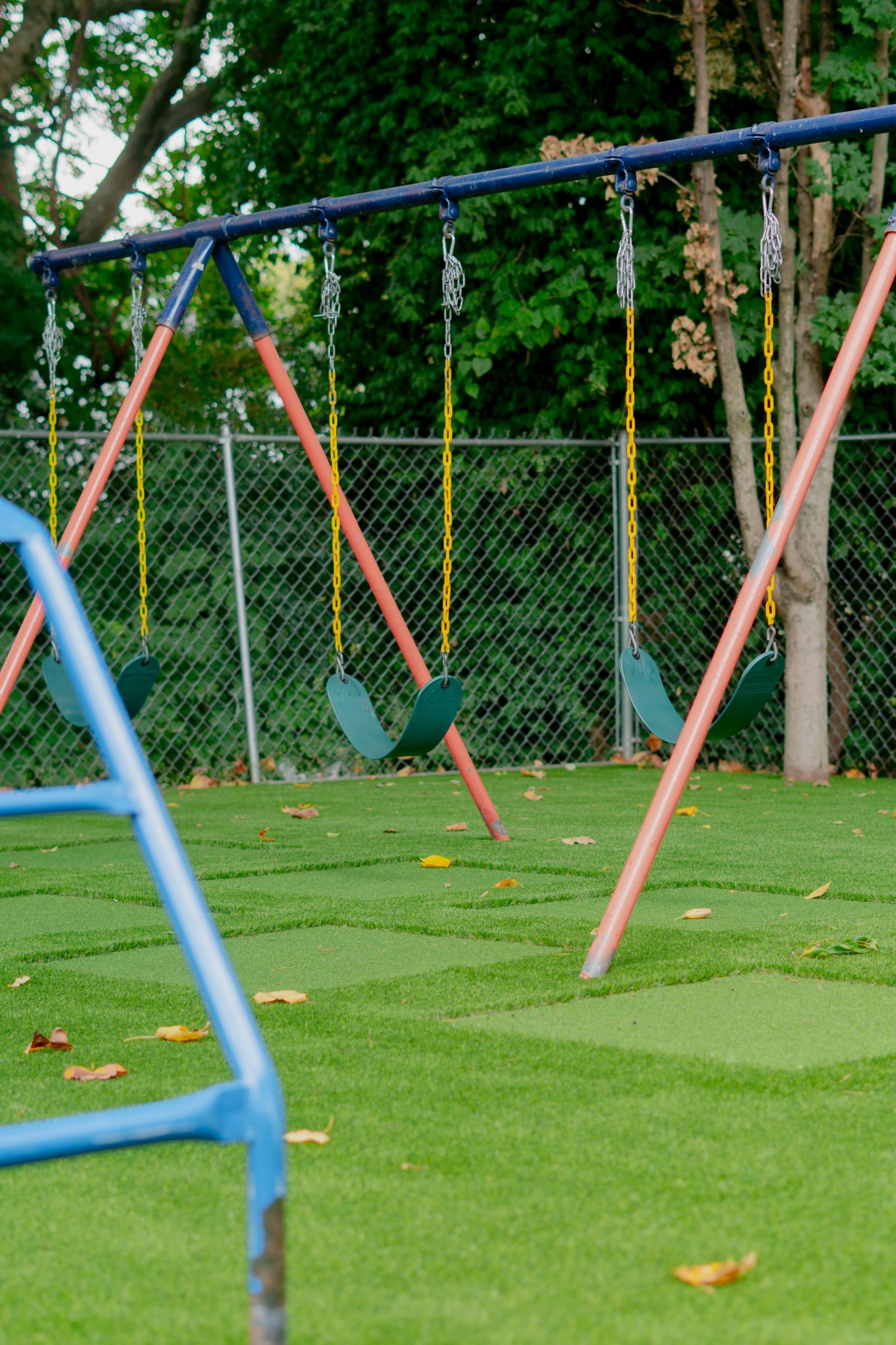 A swing set with three swings on green turf, in a park.