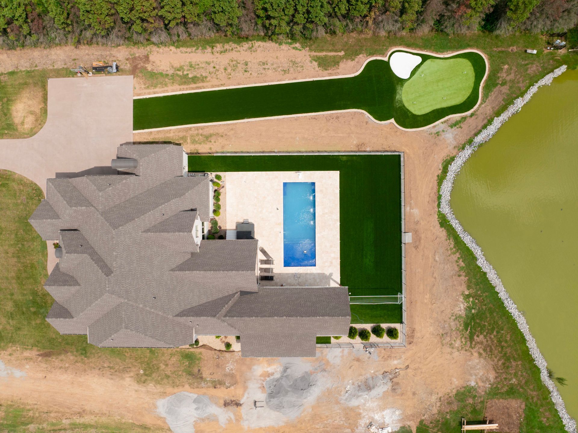 Aerial view of a house with a pool, putting green, and pond on a grassy lot.