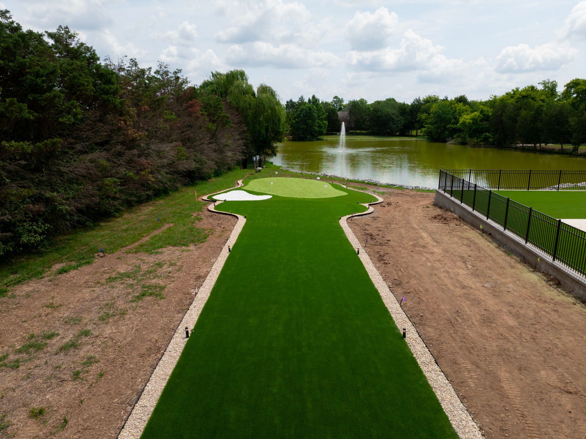 Artificial turf putting green with a pond and fountain in the background.