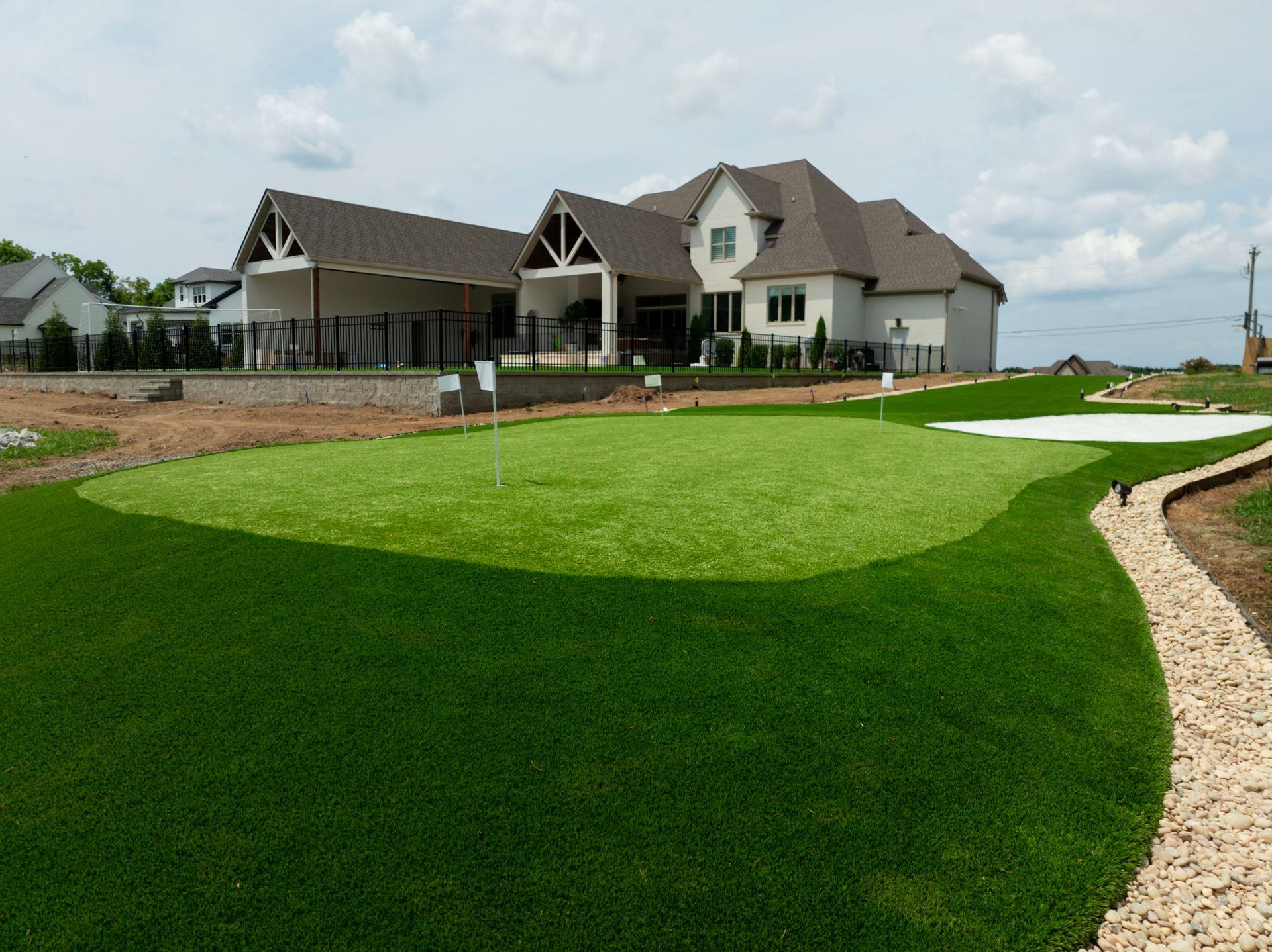 A house with a backyard putting green and stone pathway. Bright green grass contrasts with a beige house.