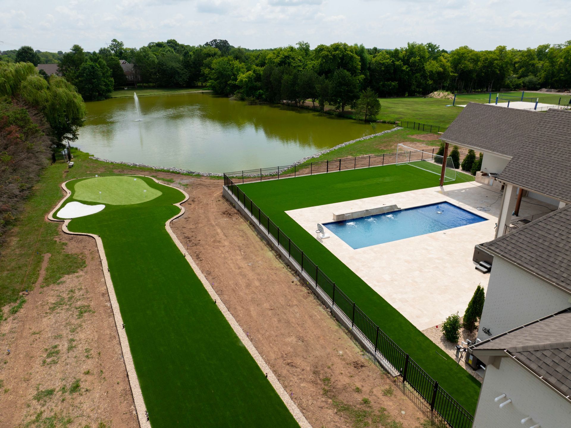 A luxury backyard with a putting green, pool, pond, and manicured lawn.