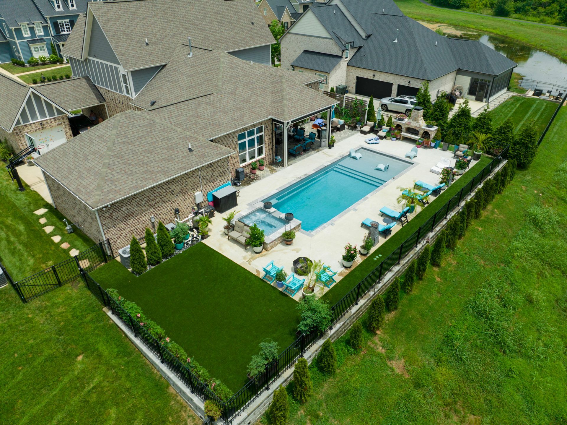 Aerial view of a luxurious home with a rectangular pool, green turf, and a black fence.