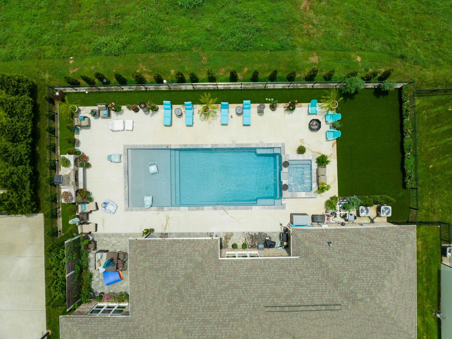 Aerial view of a backyard with a rectangular pool, lounge chairs, and green grass.