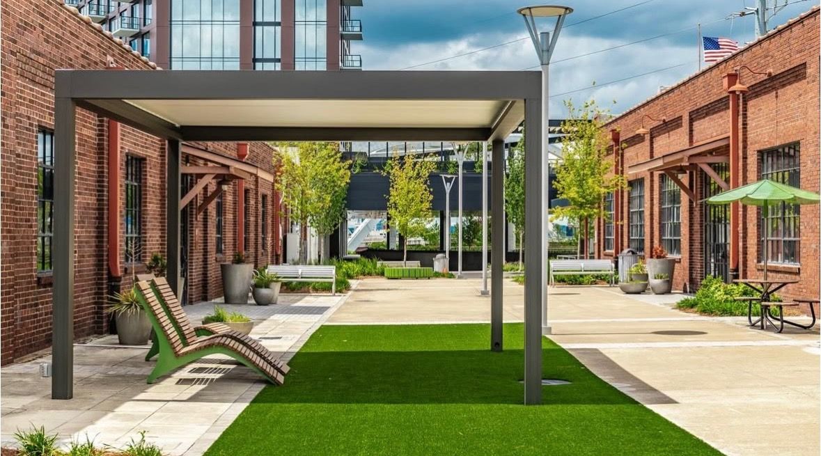 Modern outdoor space with pergola, brick buildings, green turf, and a lounge chair.