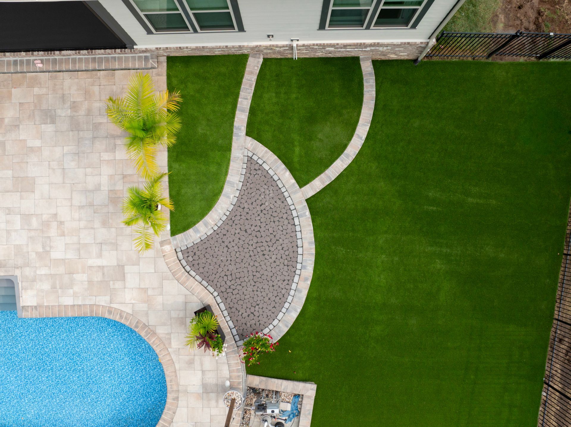 Overhead view of a backyard with a pool, patio, curved pathway, and green lawn.