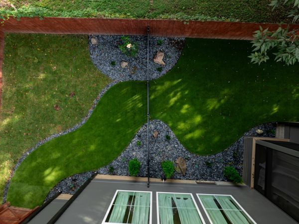 Overhead view of a backyard with a curvy green lawn, dark stone accents, and modern building.