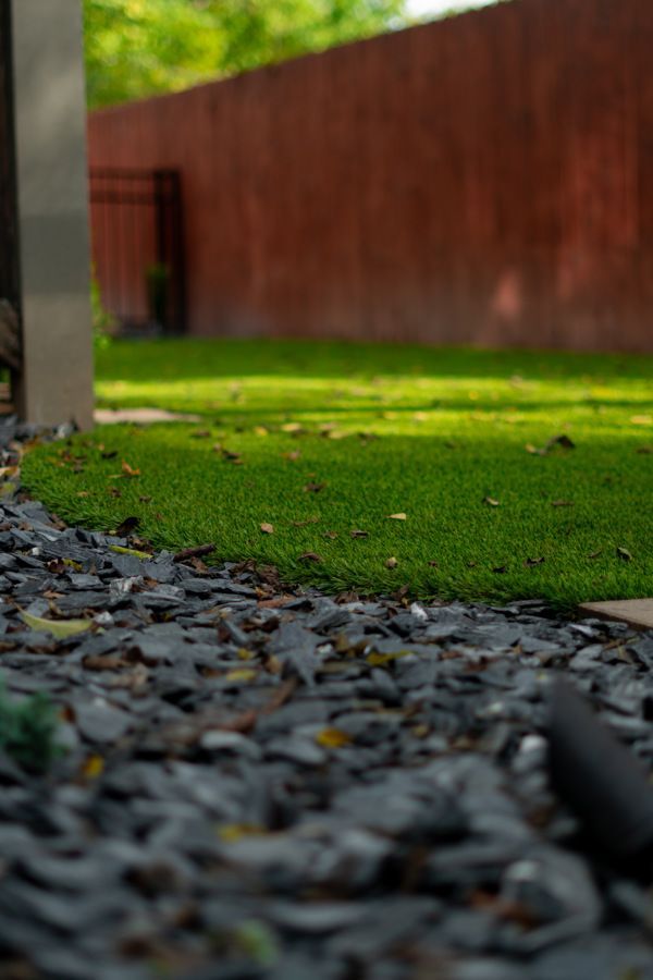 Green lawn bordered by dark gray slate, with a reddish-brown wall in the background.