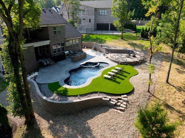 Backyard with pool, patio, and landscaping.  Dark-blue pool, green turf area, and rock retaining walls.