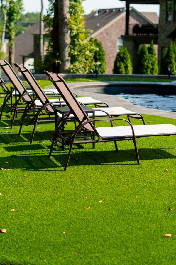 Lounge chairs on artificial green grass by a pool with a building in the background.