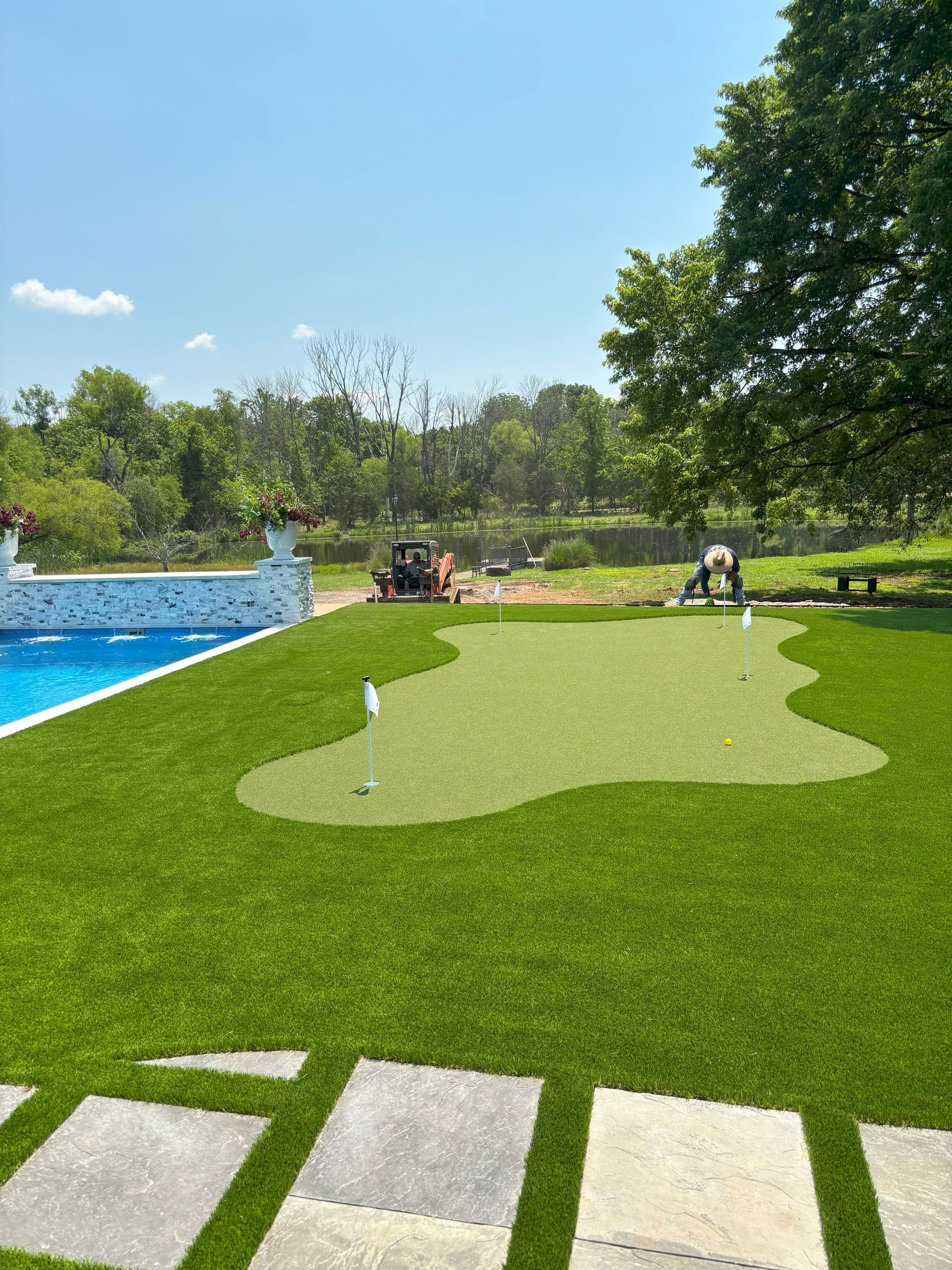 A lawn with a putting green and a pool in the background.