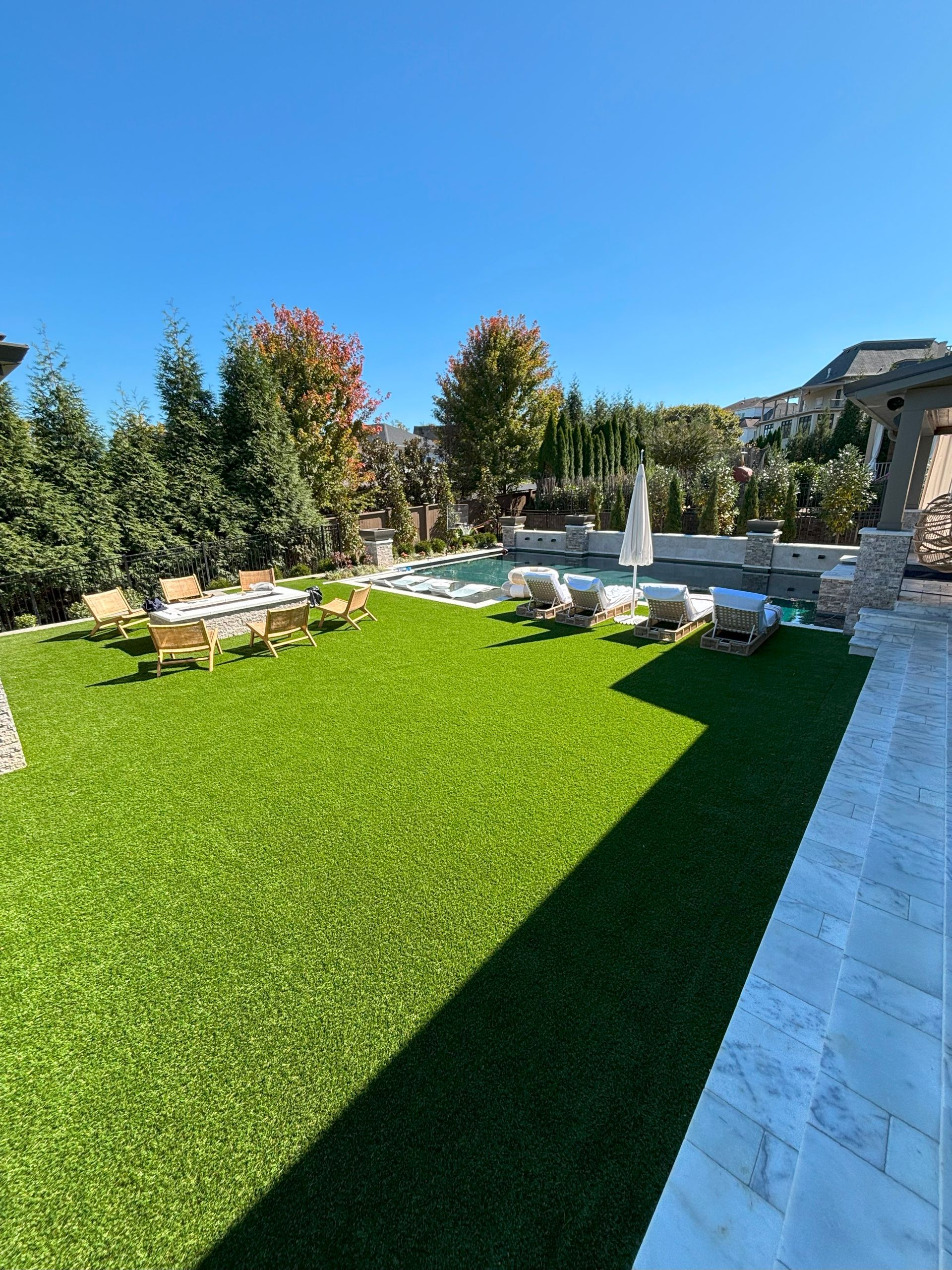 A large lawn with a swimming pool and chairs in it.