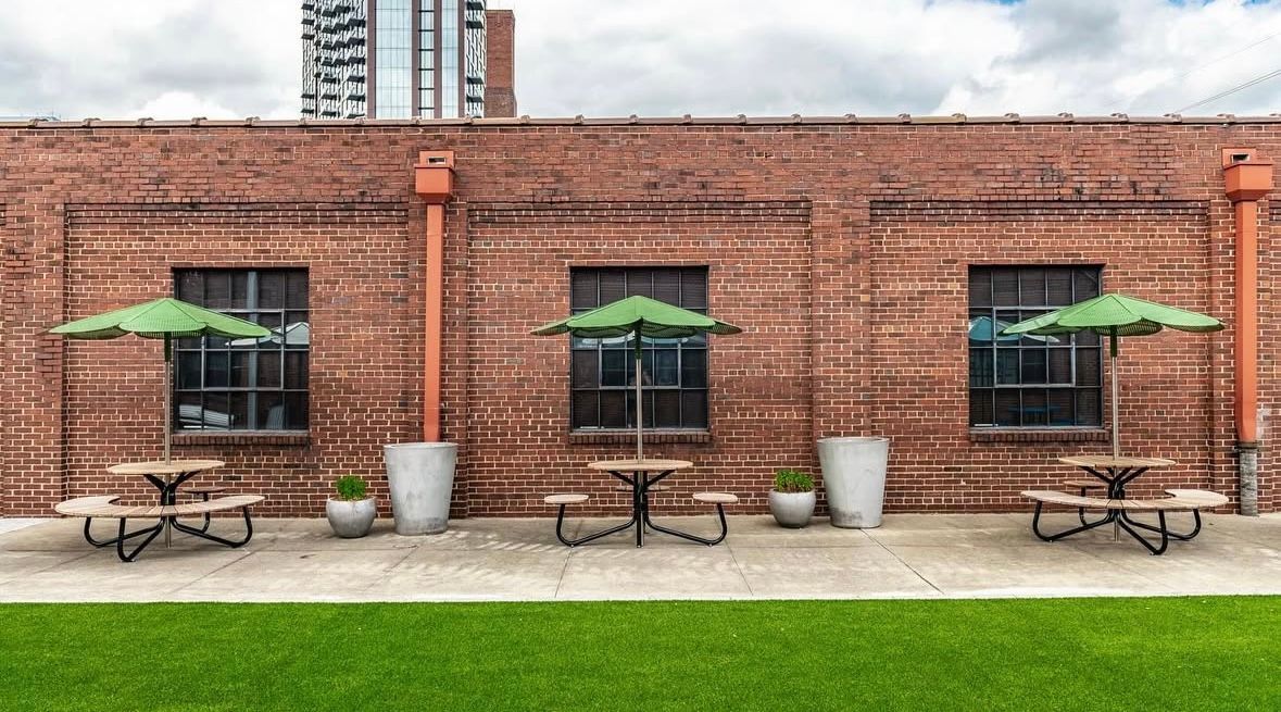 A row of picnic tables with green umbrellas in front of a brick building.