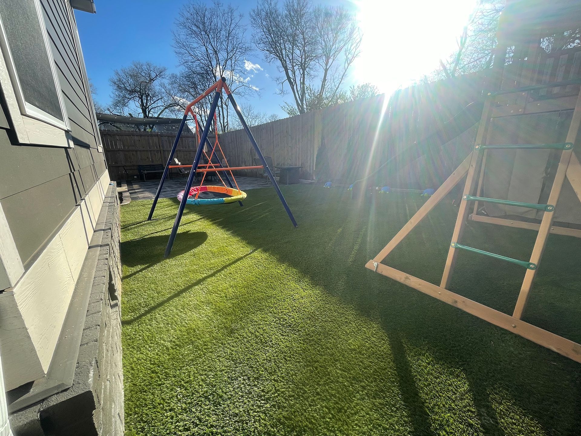 Backyard with swing set, climbing structure, and green grass, under a bright, sunny sky.