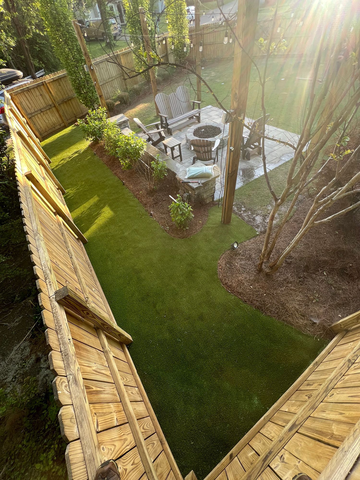 Long, narrow backyard with a green lawn, wooden fence, and a seating area.