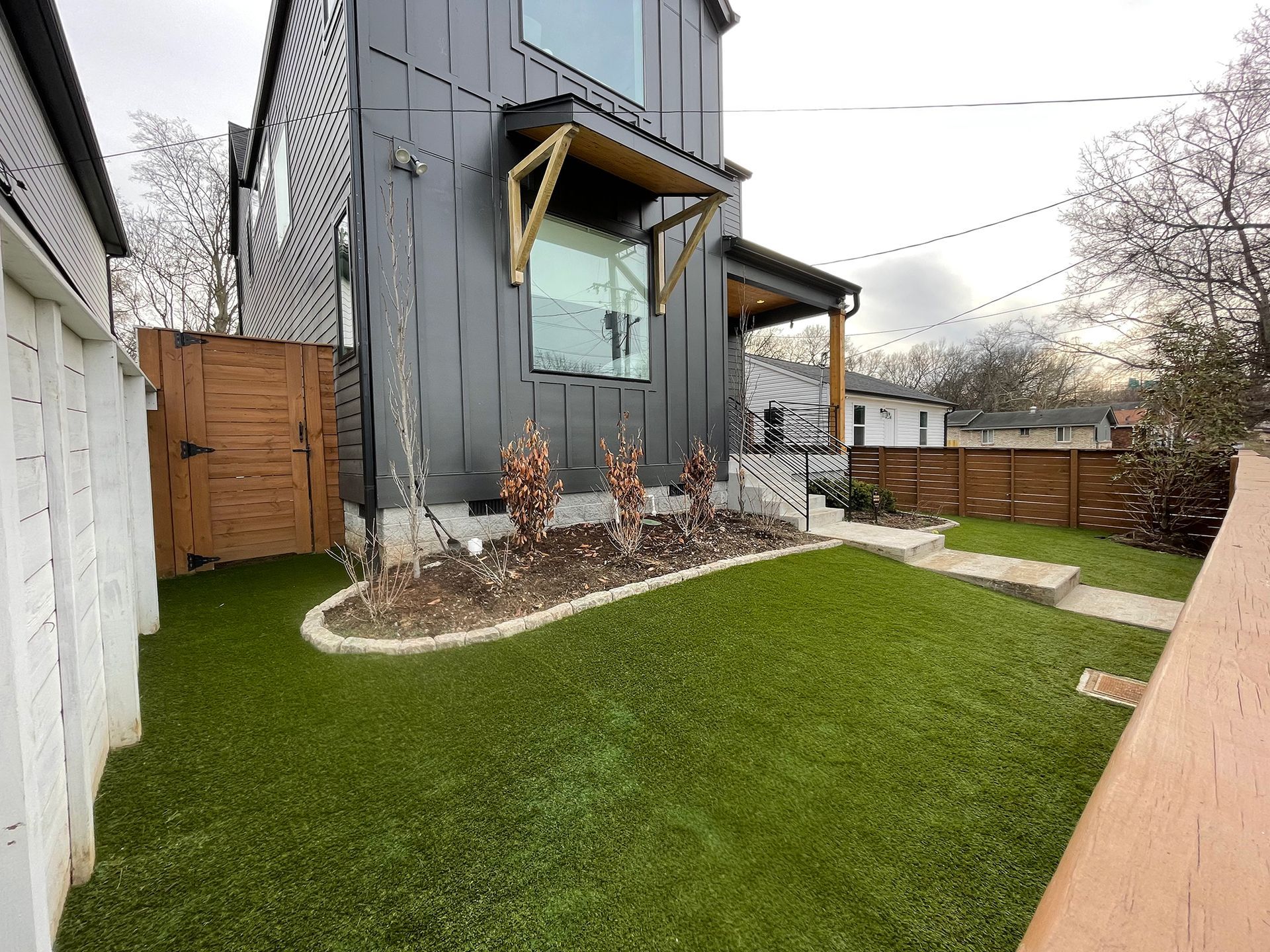 Modern black house with small yard, brown fence, and artificial green grass.