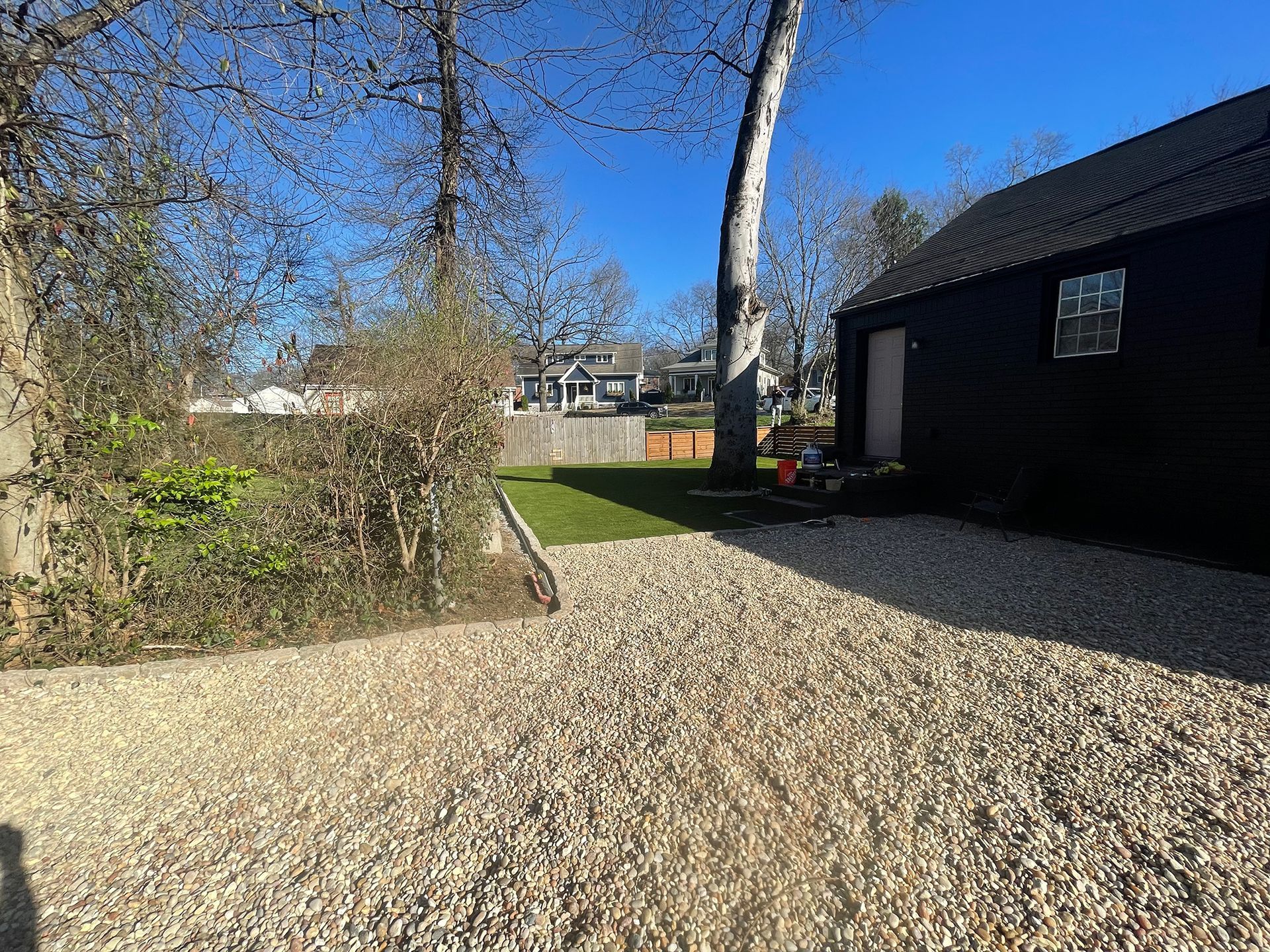 Gravel driveway leading to a black building with a door and small window, sunny outdoor setting.