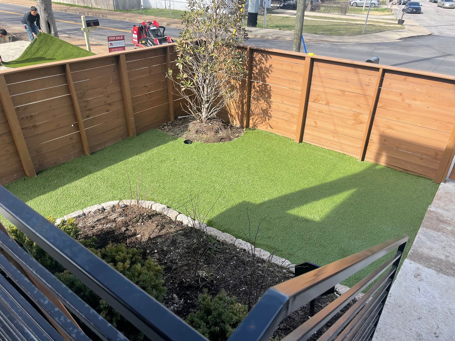 Small backyard with artificial turf, brown fence, and a young tree.
