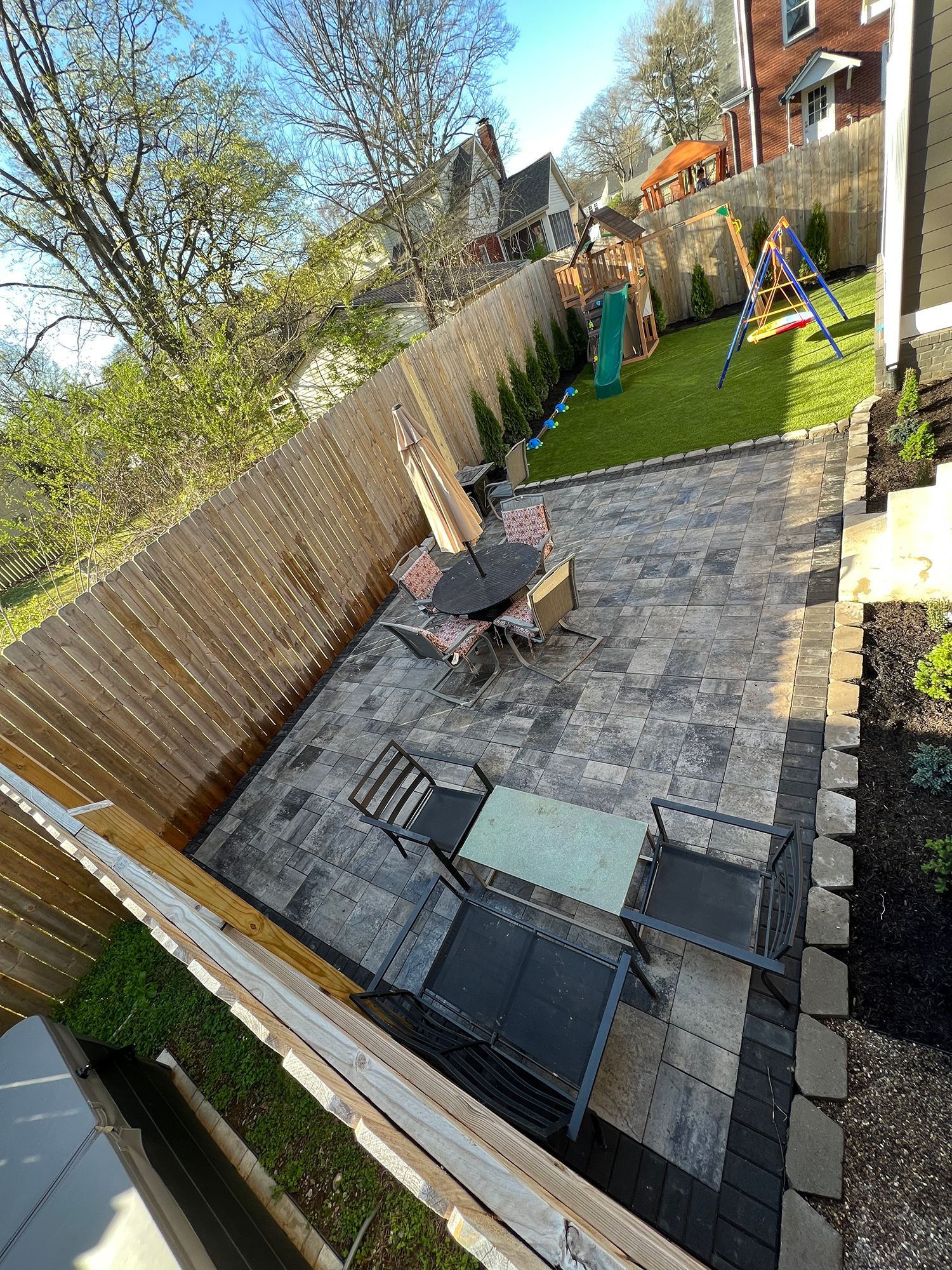 A backyard patio with seating, fire pit, and a grass play area with swing set.