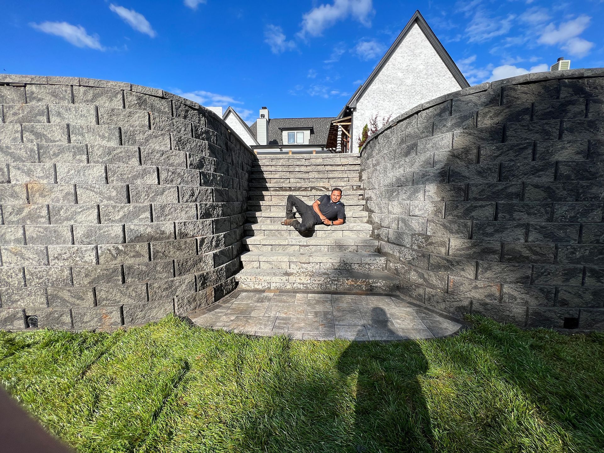 Man on stone stairs between curved retaining walls, sunny day, grass foreground, white house.