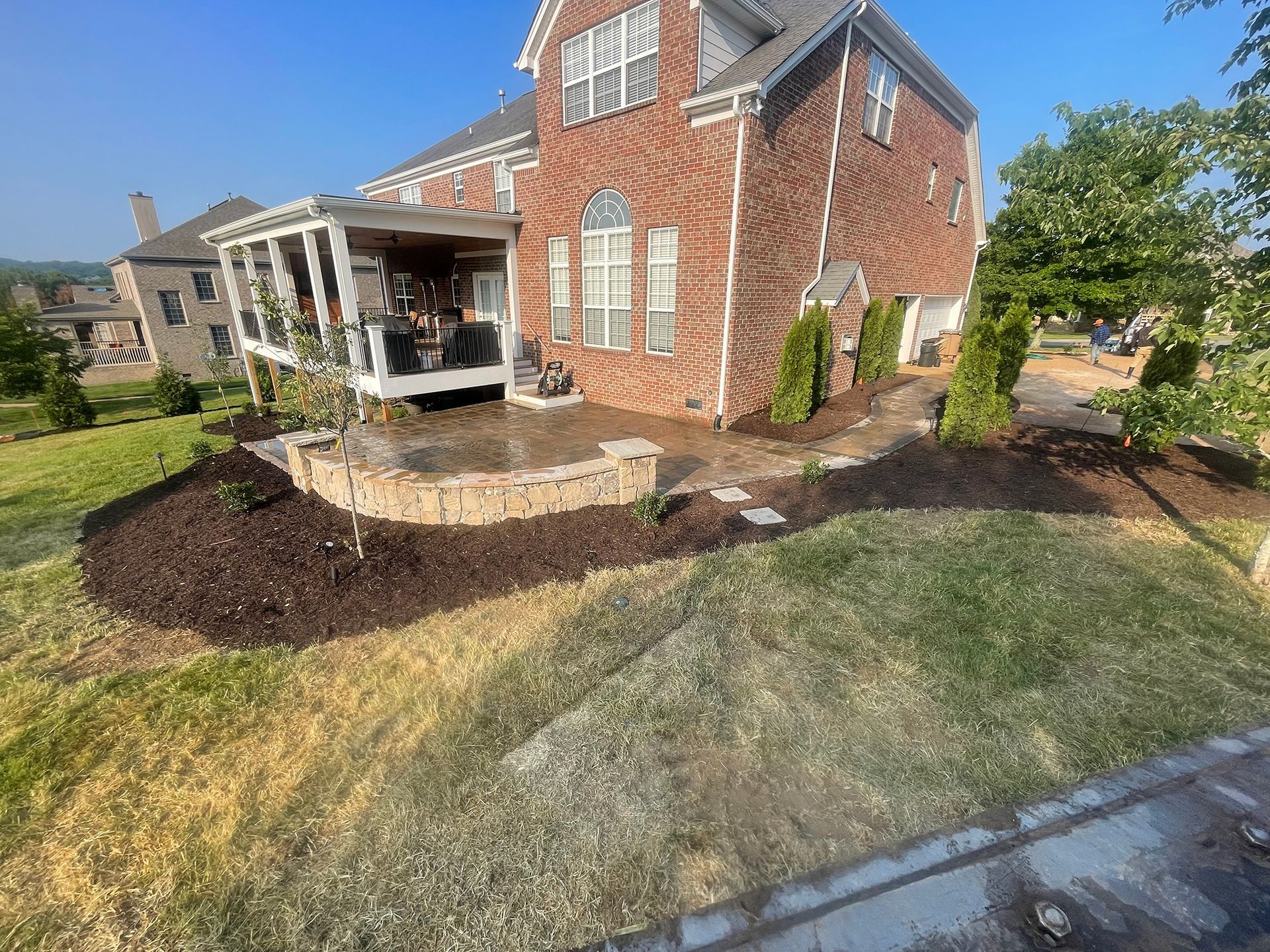 Brick house with a patio, retaining wall, and landscaping on a sunny day.