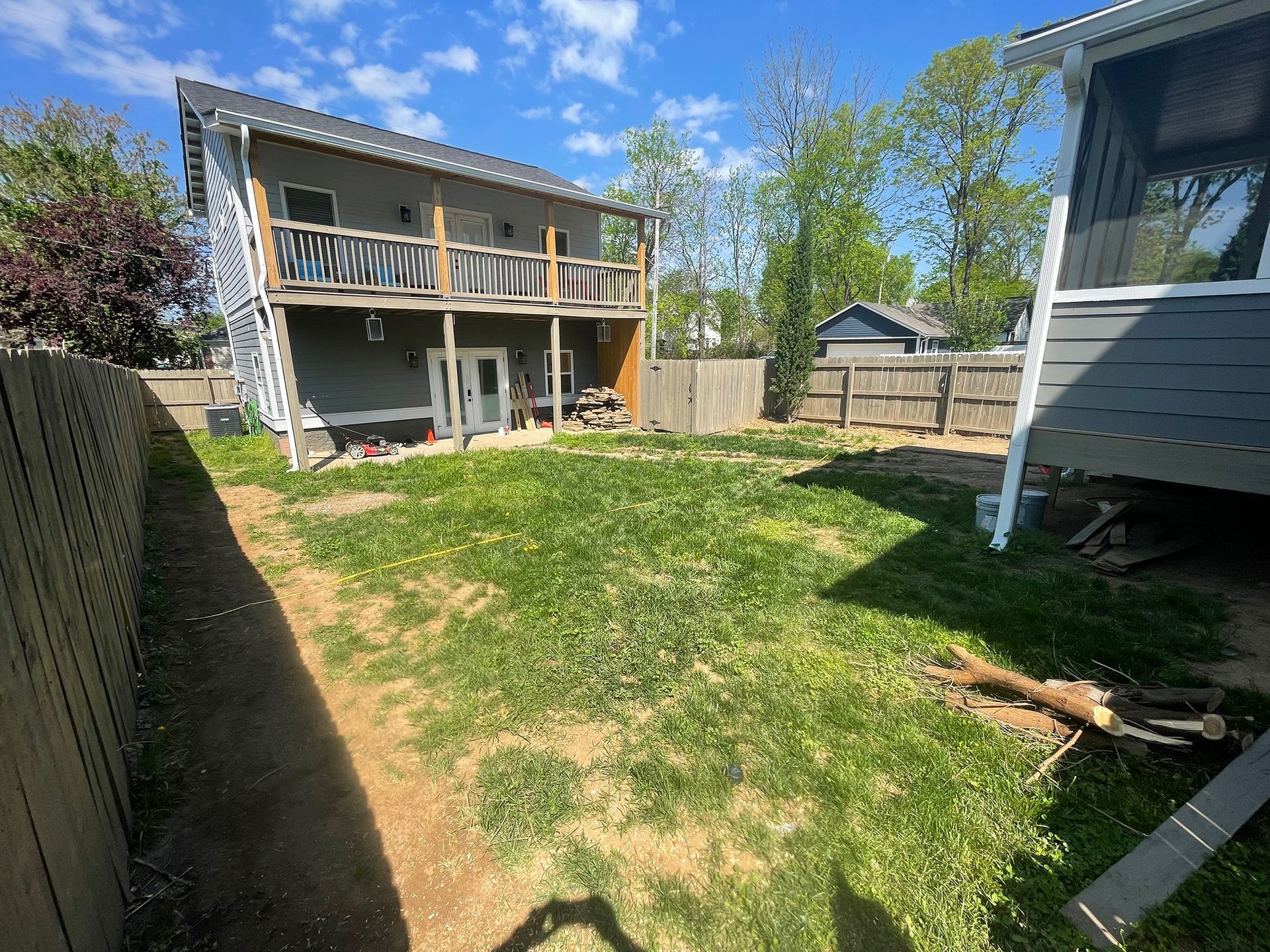 Two-story gray house with balcony overlooks a grassy backyard with wooden fences on either side.