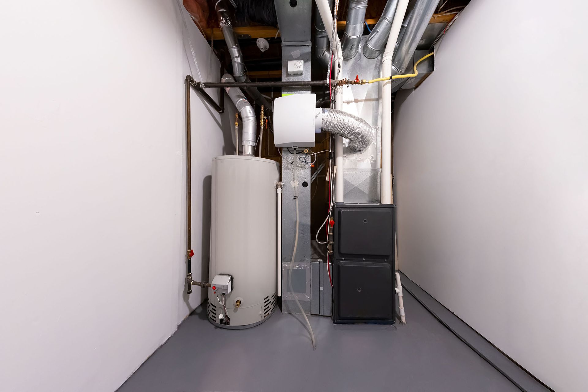 Utility room with water heater, furnace, and exposed ducts in a narrow basement utility space