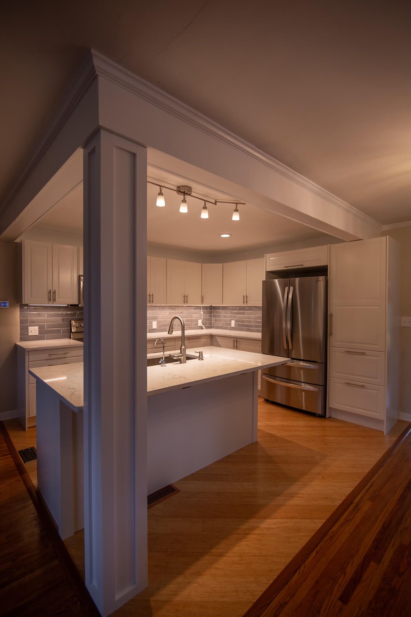 Kitchen with white cabinets, island, stainless steel refrigerator, and hardwood floors.