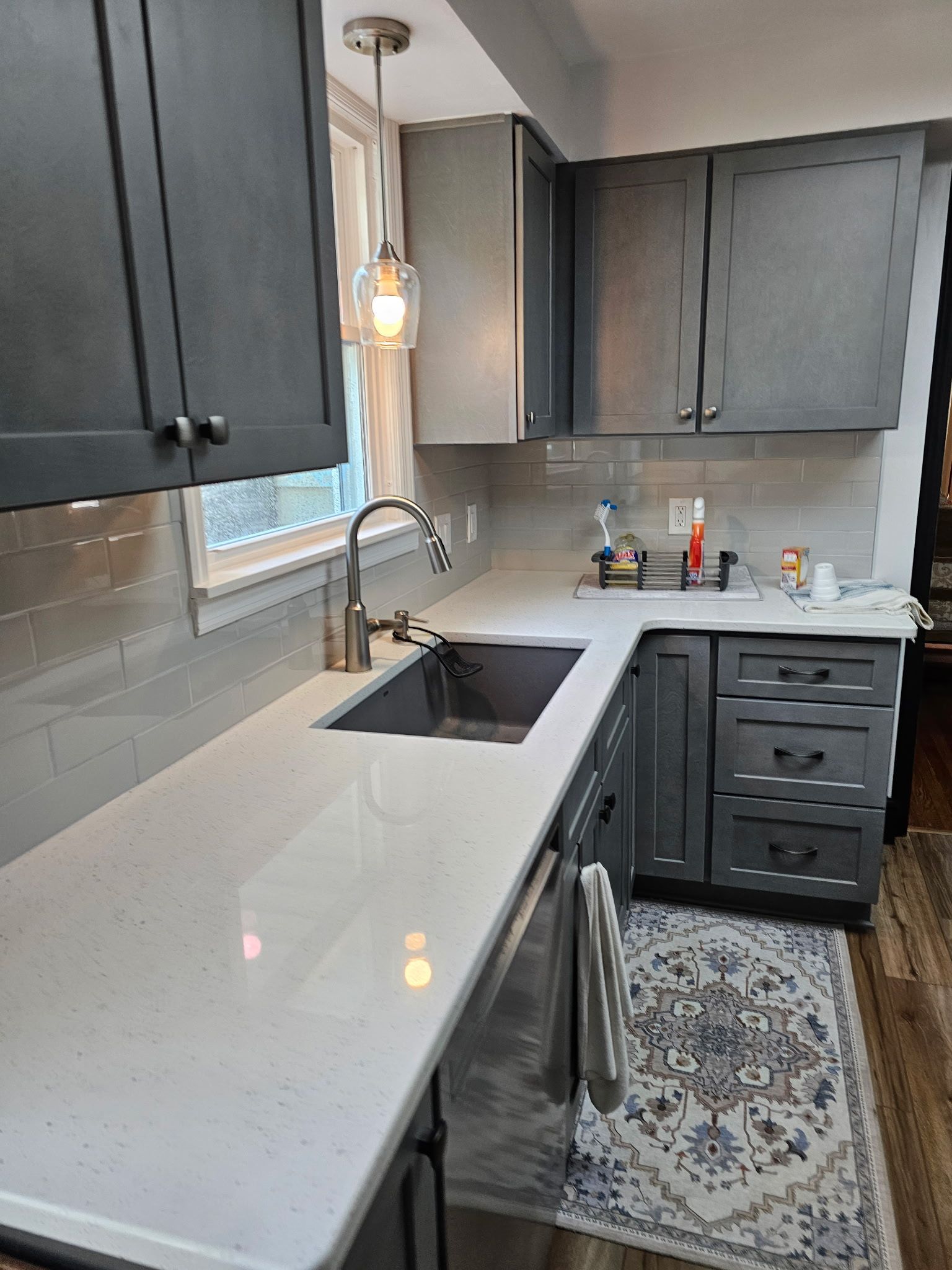 Gray and white kitchen with gray cabinets, a white countertop, and a stainless steel sink.